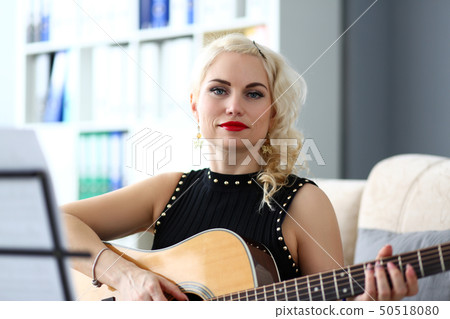 Adult beautiful woman playing acoustic guitar reading notes from stand 50518080