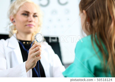 Blond mature gp hold stethoscope head in hand while diagnosing little girl Blond mature gp hold stethoscope head in hand while diagnosing little girl 50518124