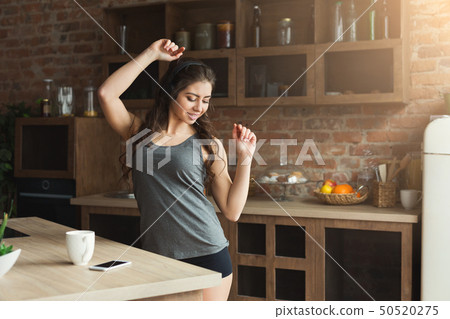 Happy young woman listening music in kitchen 50520275