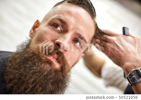 Stylish barber cuts a brutal man with a thick beard. 50521056