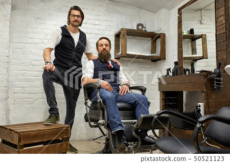 Barbershop, hairdresser and client. Hairdresser and bearded young guy posing for the camera before a 50521123