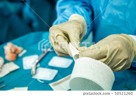 A nurse with latex gloves cuts strips of bandage in preparation to care for an injured person. A nurse with latex gloves cuts strips of bandage in preparation to care for an injured person. 50521260