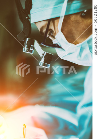 Surgeon performing surgery in hospital operating room. Surgeon in mask wearing loupes during medical 50521280