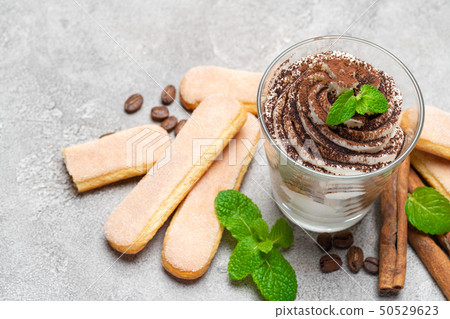 Classic tiramisu dessert in a glass and savoiardi cookies on concrete background Classic tiramisu dessert in a glass and savoiardi cookies on concrete background 50529623