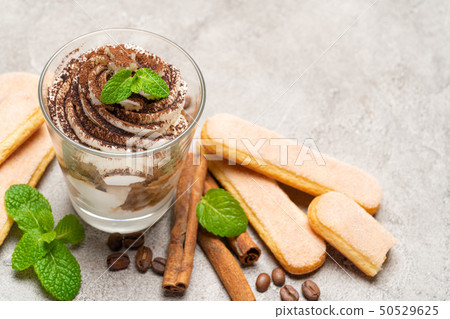 Classic tiramisu dessert in a glass and savoiardi cookies on concrete background Classic tiramisu dessert in a glass and savoiardi cookies on concrete background 50529625