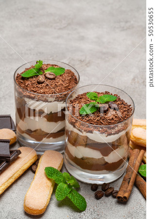 Classic tiramisu dessert in a glass and savoiardi cookies on concrete background Classic tiramisu dessert in a glass and savoiardi cookies on concrete background 50530655