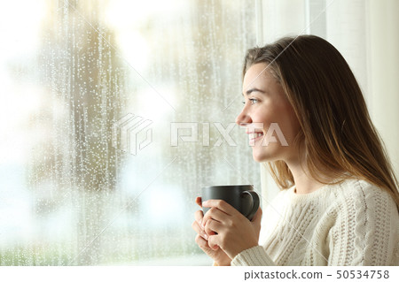Happy teen holding a mug looking through a window 50534758