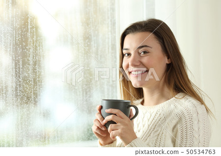 Happy teen holding a coffee mug posing in a rainy 50534763