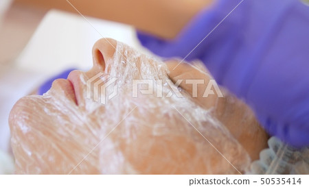 The concept of a beautician. The hands of a cosmetologist put a film on the face of a woman The concept of a beautician. The hands of a cosmetologist put a film on the face of a woman 50535414