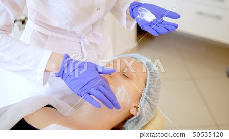 concept beautician. The hands of a cosmetologist put cream on the face of a woman. Beautician 50535420
