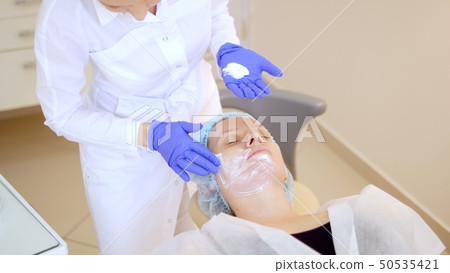 concept beautician. The hands of a cosmetologist put cream on the face of a woman. Beautician 50535421