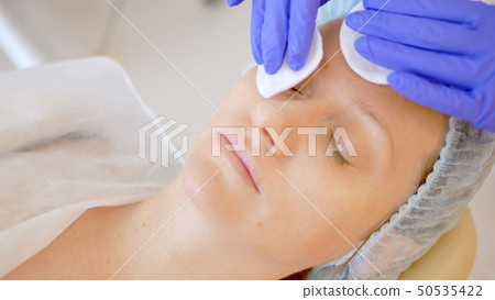 The concept of a beautician. The hands of a cosmetologist apply lotion with a cotton pad on the face 50535422