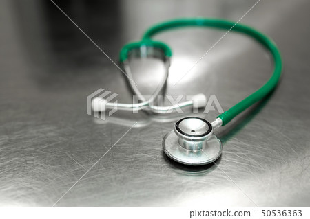 A green stethoscope is lying on a metal table in a 50536363