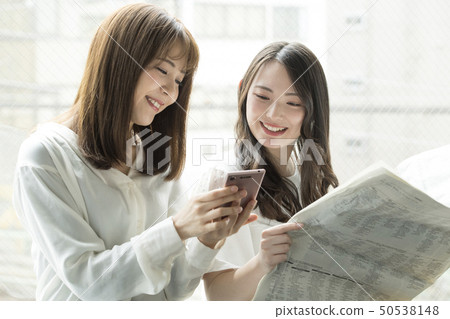在窗口邊觀看智能手機和報紙的兩名婦女 在窗口邊觀看智能手機和報紙的兩名婦女 50538148