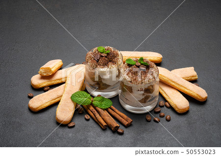 Classic tiramisu dessert in a glass and savoiardi cookies on dark concrete background 50553023