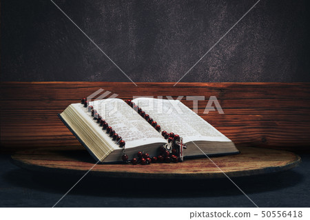 Bible and the crucifix beads on a old round table. Bible and the crucifix beads on a old round table. 50556418