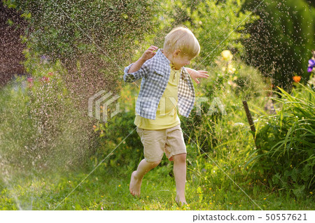 Funny little boy playing with garden sprinkler in Funny little boy playing with garden sprinkler in 50557621