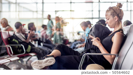 Female traveler using her cell phone while waiting to board a plane at departure gates at asian Female traveler using her cell phone while waiting to board a plane at departure gates at asian 50564602