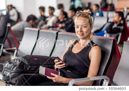 Casual tanned blond female traveler holding cell phone, passport and boarding pass while waiting to Casual tanned blond female traveler holding cell phone, passport and boarding pass while waiting to 50564603