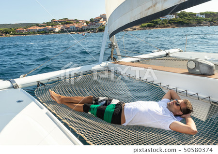 Sporty man relaxing on a luxury catamaran sailing boat. Sporty man relaxing on a luxury catamaran sailing boat. 50580374