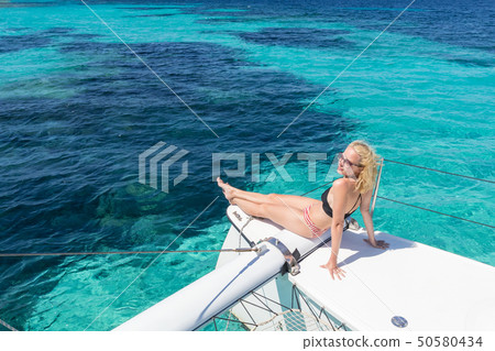 Woman relaxing on a summer sailing cruise, sitting on a luxury catamaran near picture perfect white Woman relaxing on a summer sailing cruise, sitting on a luxury catamaran near picture perfect white 50580434