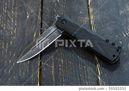 Black knife in the folded form. Wooden background. 50583203
