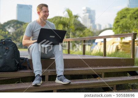 Young happy man thinking while using laptop on wooden bridge at the park Young happy man thinking while using laptop on wooden bridge at the park 50588696