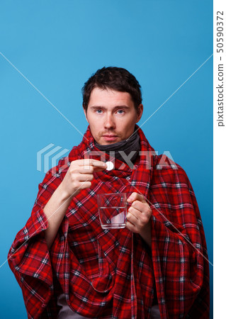 A wrapped in a blanket sick man with tablet and mug. 50590372