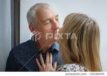 Hot and Sexy Middle-aged Woman Kissing Her Elderly Husband inside Their Home. Couple with Age Hot and Sexy Middle-aged Woman Kissing Her Elderly Husband inside Their Home. Couple with Age 50590444
