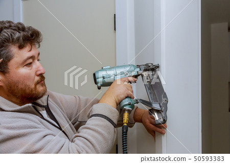 Carpenter using nail gun to moldings on door, framing trim, 50593383