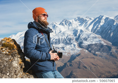 Portrait of a bearded traveler photographer in sunglasses and a cap sits on a rock with mirror Portrait of a bearded traveler photographer in sunglasses and a cap sits on a rock with mirror 50607065