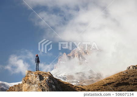 A traveler is a man with a beard and a hat standing on a rock at the foot of epic rocks partly A traveler is a man with a beard and a hat standing on a rock at the foot of epic rocks partly 50607134