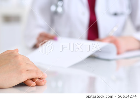 Unknown doctor woman consulting patient while filling up an application form at the desk in hospital 50614274