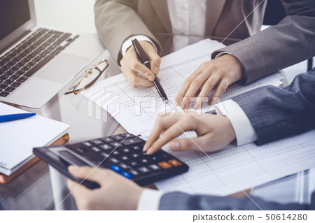 Two female accountants counting on calculator income for tax form completion hands close-up 50614280