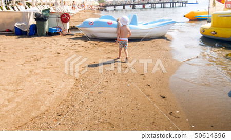 Rera view image of little toddler boy walking on sea beach toward boats and catamarans Rera view image of little toddler boy walking on sea beach toward boats and catamarans 50614896