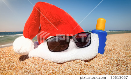 Closeup image of Santa's hat with sunglasses and sun lotion on sandy sea beach. Concept of travel Closeup image of Santa's hat with sunglasses and sun lotion on sandy sea beach. Concept of travel 50615067