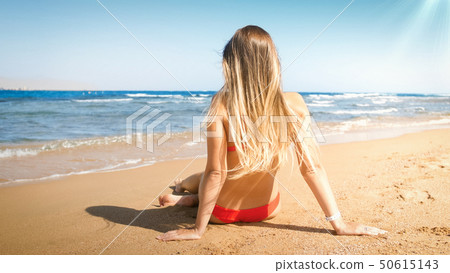 Sexy young woman with long hair wearing red bikini sitting on the beach 50615143
