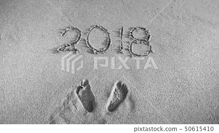 Black and white image of footprints and 2018 numbers written on sand beach. Concept of celebrating Black and white image of footprints and 2018 numbers written on sand beach. Concept of celebrating 50615410