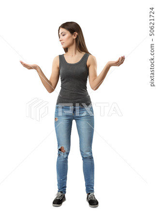 Young woman in gray top and blue jeans standing with arms bent and raised at sides looking at one of Young woman in gray top and blue jeans standing with arms bent and raised at sides looking at one of 50621724