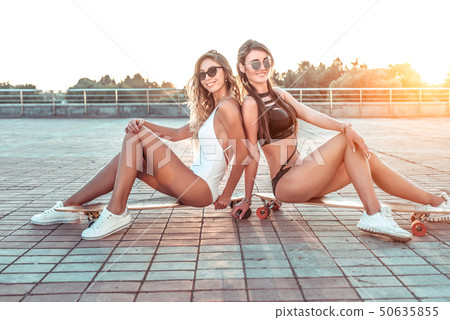 Two girlfriends girl posing, background tiles, summer city, skate board, casual wear swimsuit. Happy Two girlfriends girl posing, background tiles, summer city, skate board, casual wear swimsuit. Happy 50635855