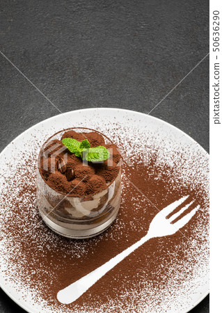 Classic tiramisu dessert in a glass on plate with fork silhouette on dark concrete background 50636290