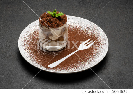 Classic tiramisu dessert in a glass on plate with fork silhouette on dark concrete background Classic tiramisu dessert in a glass on plate with fork silhouette on dark concrete background 50636293