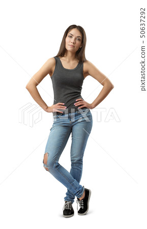 Young woman in gray sleeveless top and blue jeans standing with hands on hips and one leg in front 50637292