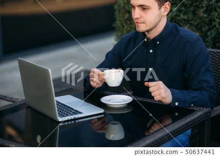 Handsome man drink cappuchino in cafe on the terrace and look into his laptop 50637441
