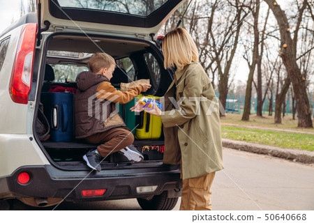 little kid sitting with mother in car trunk full of luggage eating chocolate candies little kid sitting with mother in car trunk full of luggage eating chocolate candies 50640668