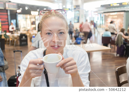 Portrait of a casual young blond woman having a cup of coffee, sitting in cafe indoors of an airport 50642212