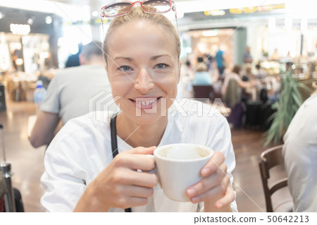 Portrait of a casual young blond woman having a cup of coffee, sitting in cafe indoors of an airport 50642213