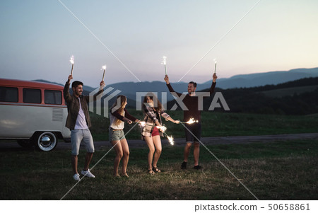 A group of friends with sparklers standing outdoors at dusk. 50658861
