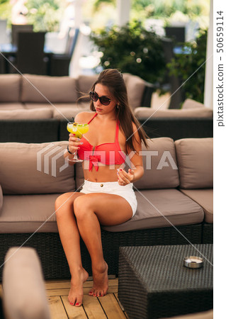 Beautiful young woman wearing swimsuit drinking a colorful cocktail sitting on a cabin of the beach 50659114