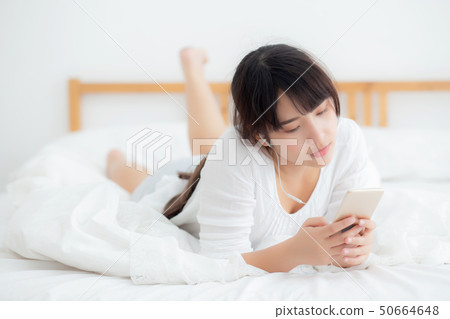 Asian woman lying listening music on phone Asian woman lying listening music on phone 50664648